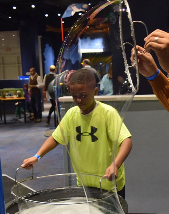 A boy creates a giant bubble at a hands-on exhibit in a children's science center, exploring STEM.