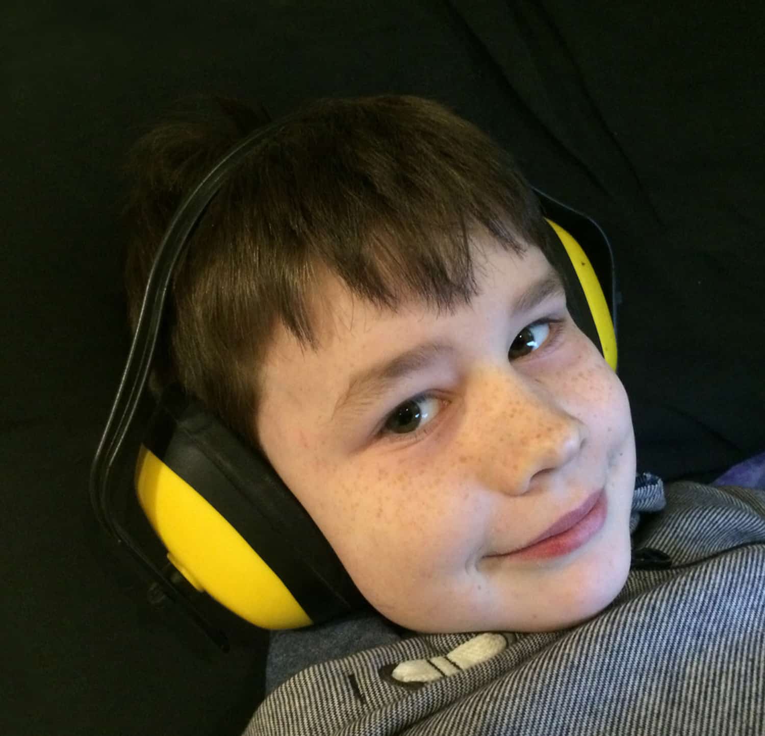 A child wearing yellow noise-canceling headphones smiles during a sensory-friendly science exhibit at the children's museum.