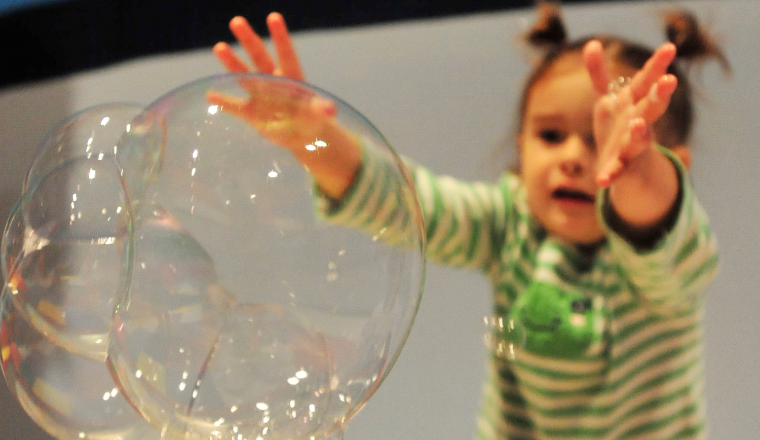 A child reaches for giant soap bubbles at a children's science center bubble exhibit, hands-on STEM play.