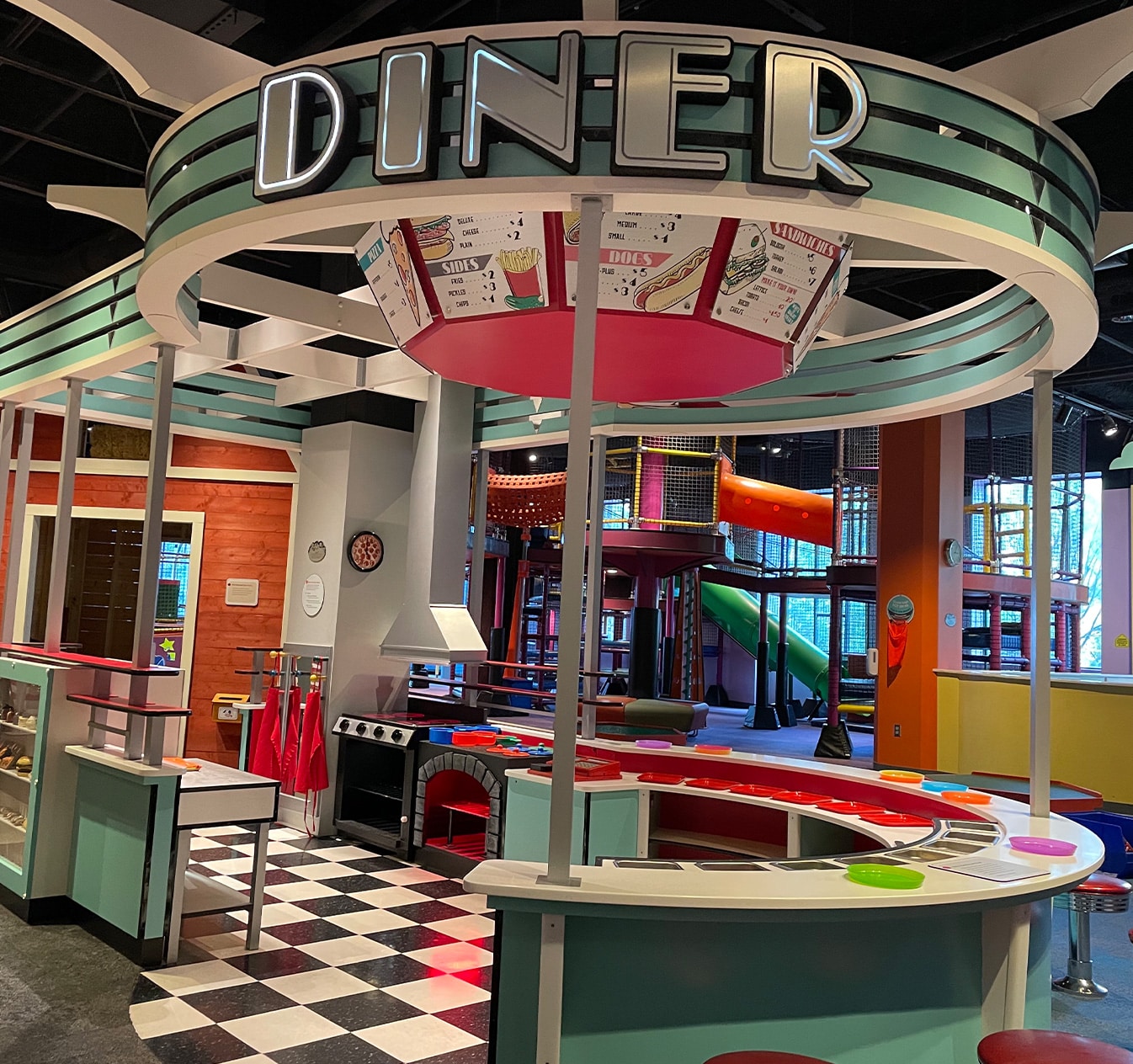 Interactive diner exhibit at children's science center with pretend kitchen and indoor playground slides.