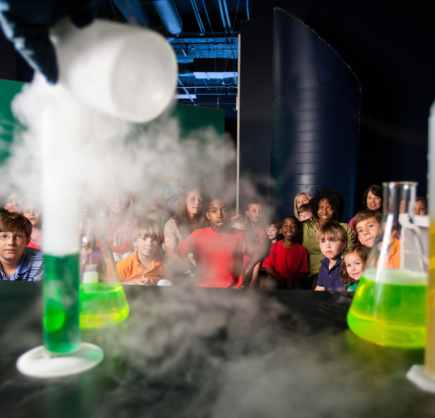 Children watch a smoky chemistry experiment with green beakers at a children's science center STEM show.