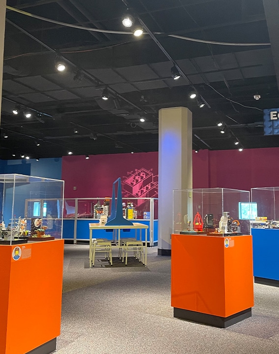 Kids science center gallery with STEM exhibits in glass cases, orange pedestals, and hands-on stations.