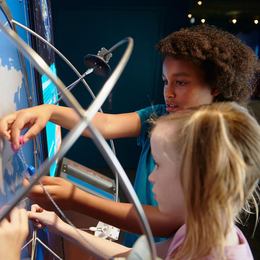 Children exploring a hands-on STEM exhibit at a science center, mapping routes on a world display