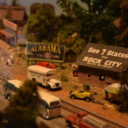 Model train diorama at children’s science center with Alabama sign, Rock City barn, vintage buses, cars, and railroad tracks