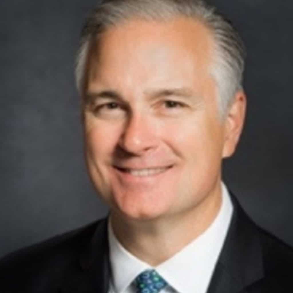 A man in a suit smiling against a dark backdrop, Children’s Science Center leadership team headshot for STEM education.