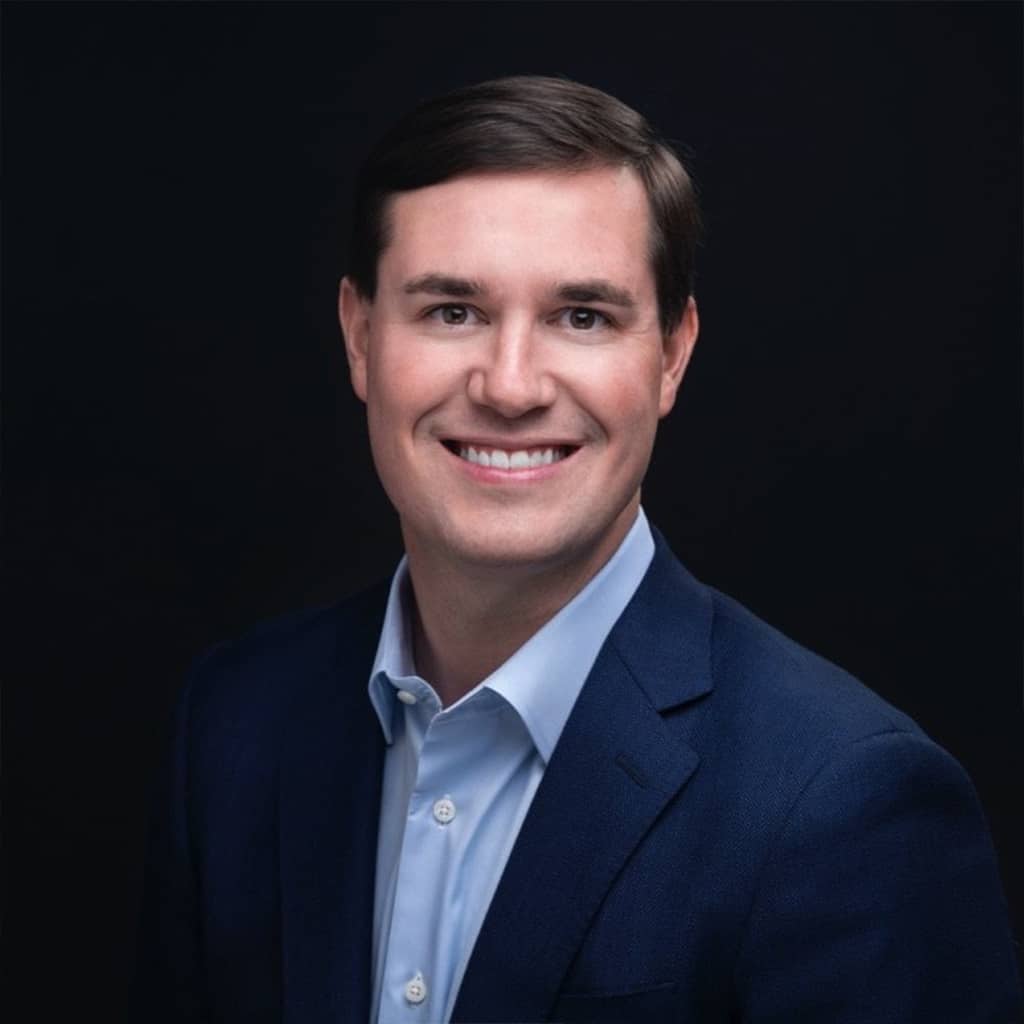 Smiling man in navy suit, children's science center leadership headshot on black background