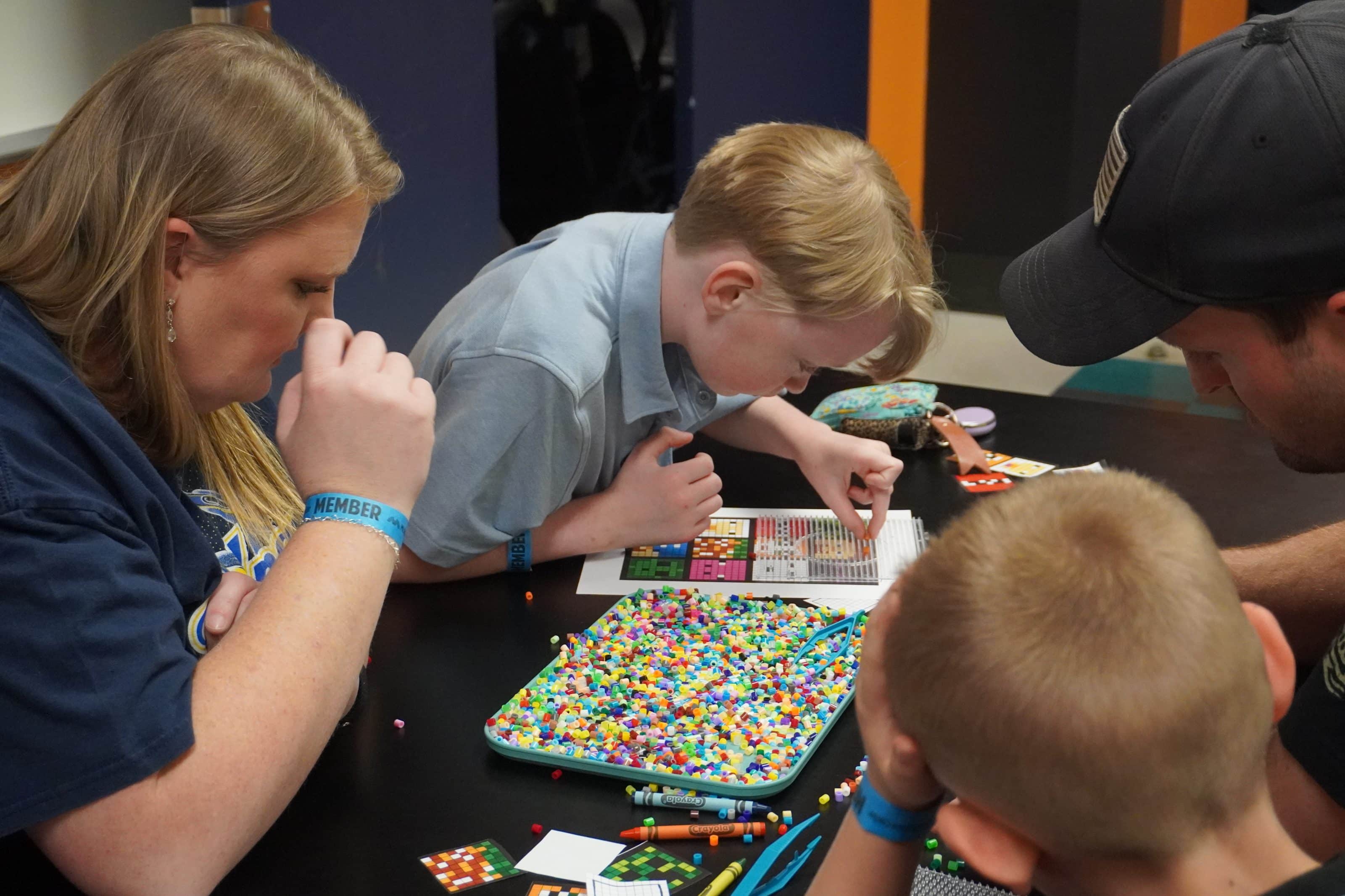 Kids and adults build pixel art with colorful beads during a hands-on STEAM activity at a children's science center.