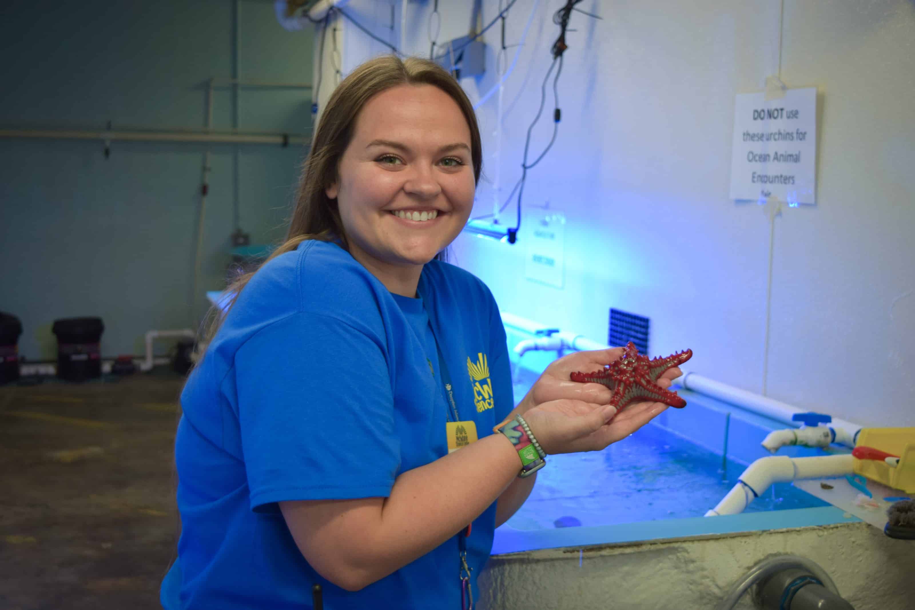 A woman holds a red sea star at a children's science center aquarium touch tank, hands-on marine science learning.