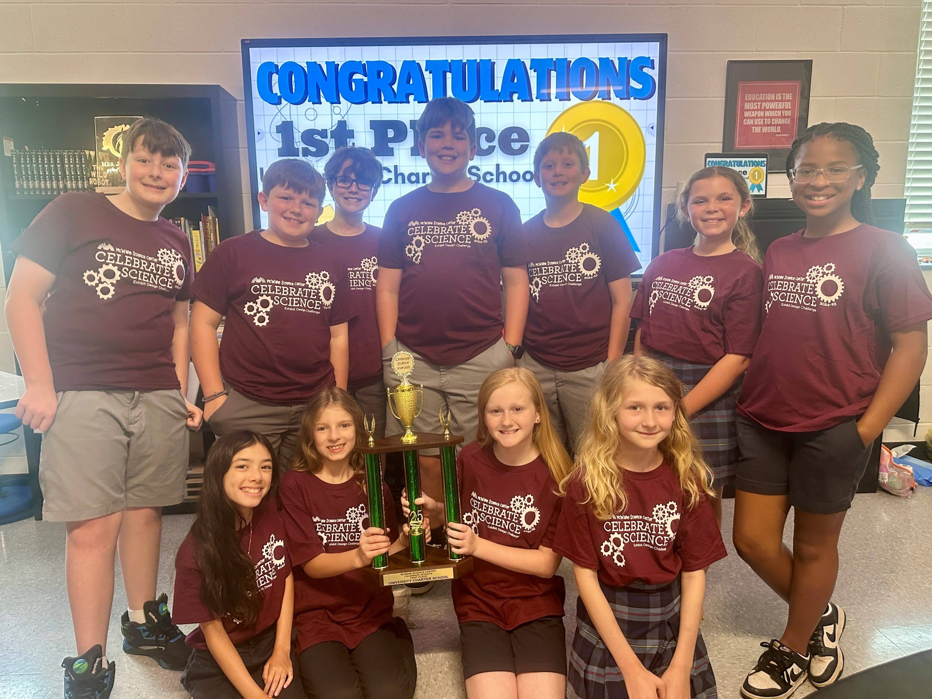 Students celebrate 1st place STEM trophy at children's science center event, wearing Celebrate Science shirts in classroom