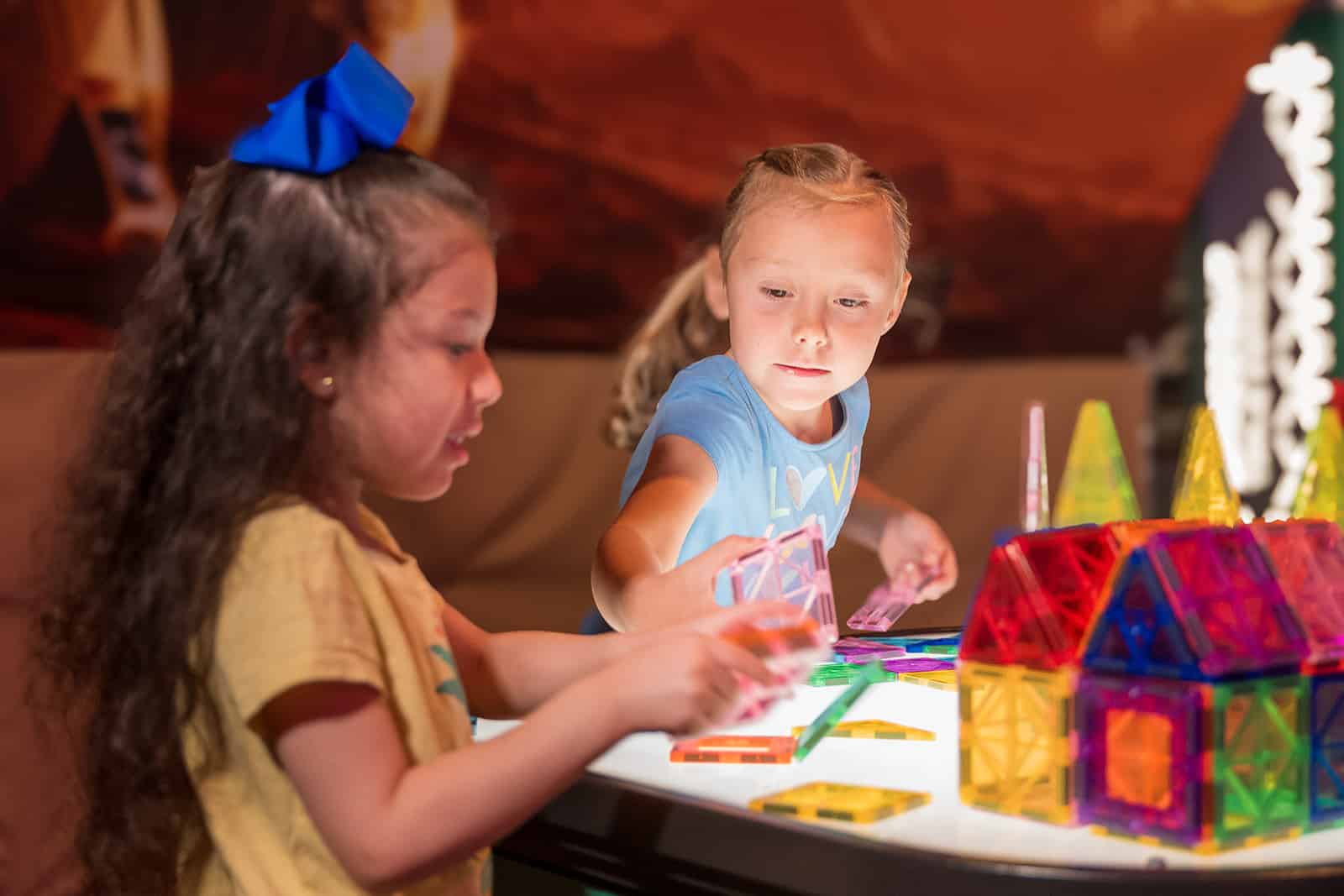 Two children exploring magnetic tiles at a light table in an interactive STEM exhibit at a children's science center.