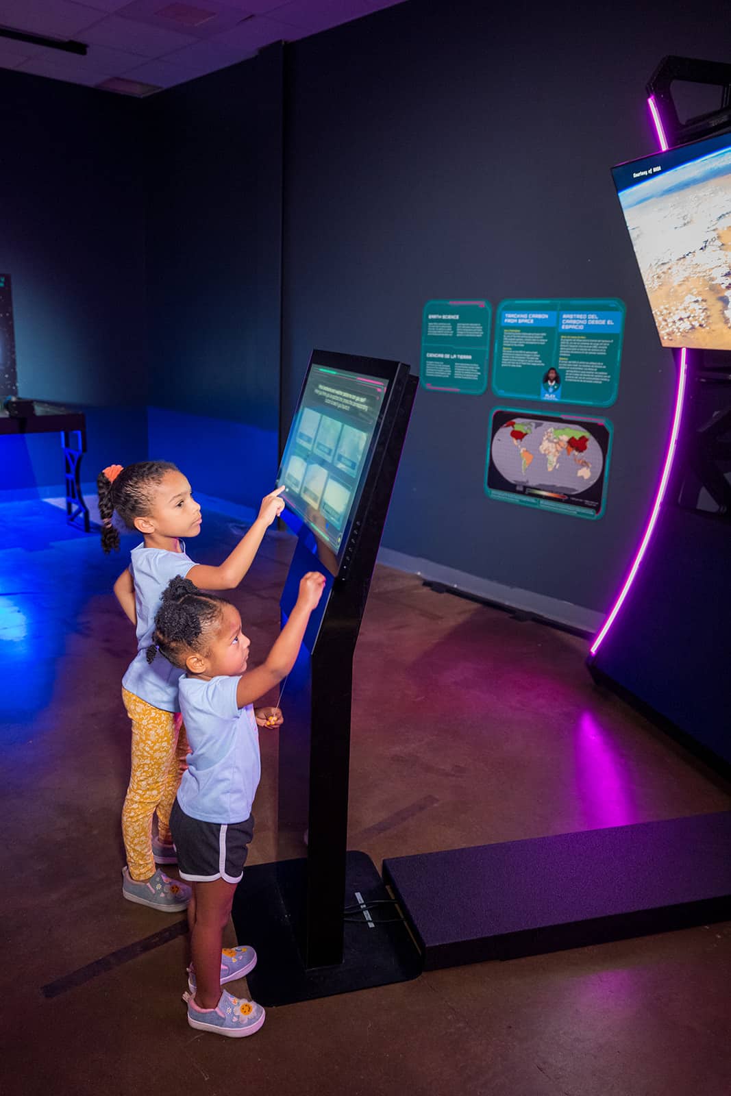 Two children using an interactive touchscreen at a children's science center exhibit about Earth science and space.
