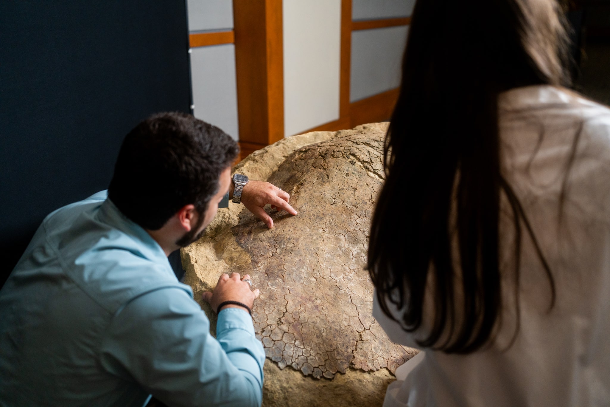 Two people examine a dinosaur fossil shell at a children's science center hands-on exhibit