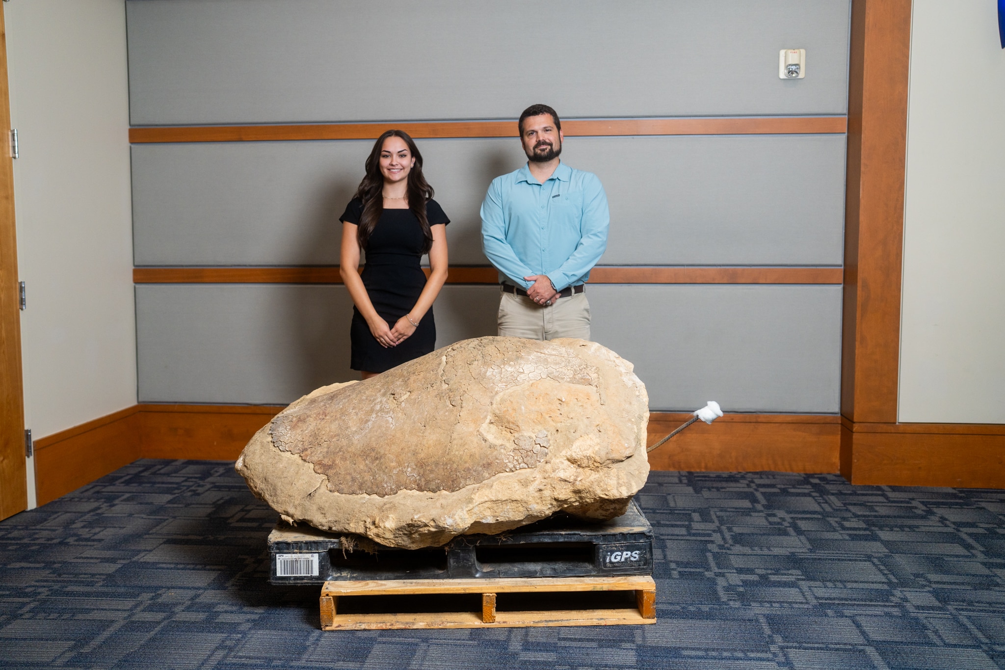 Two people with a giant rock specimen on a pallet at a children's science center geology exhibit.