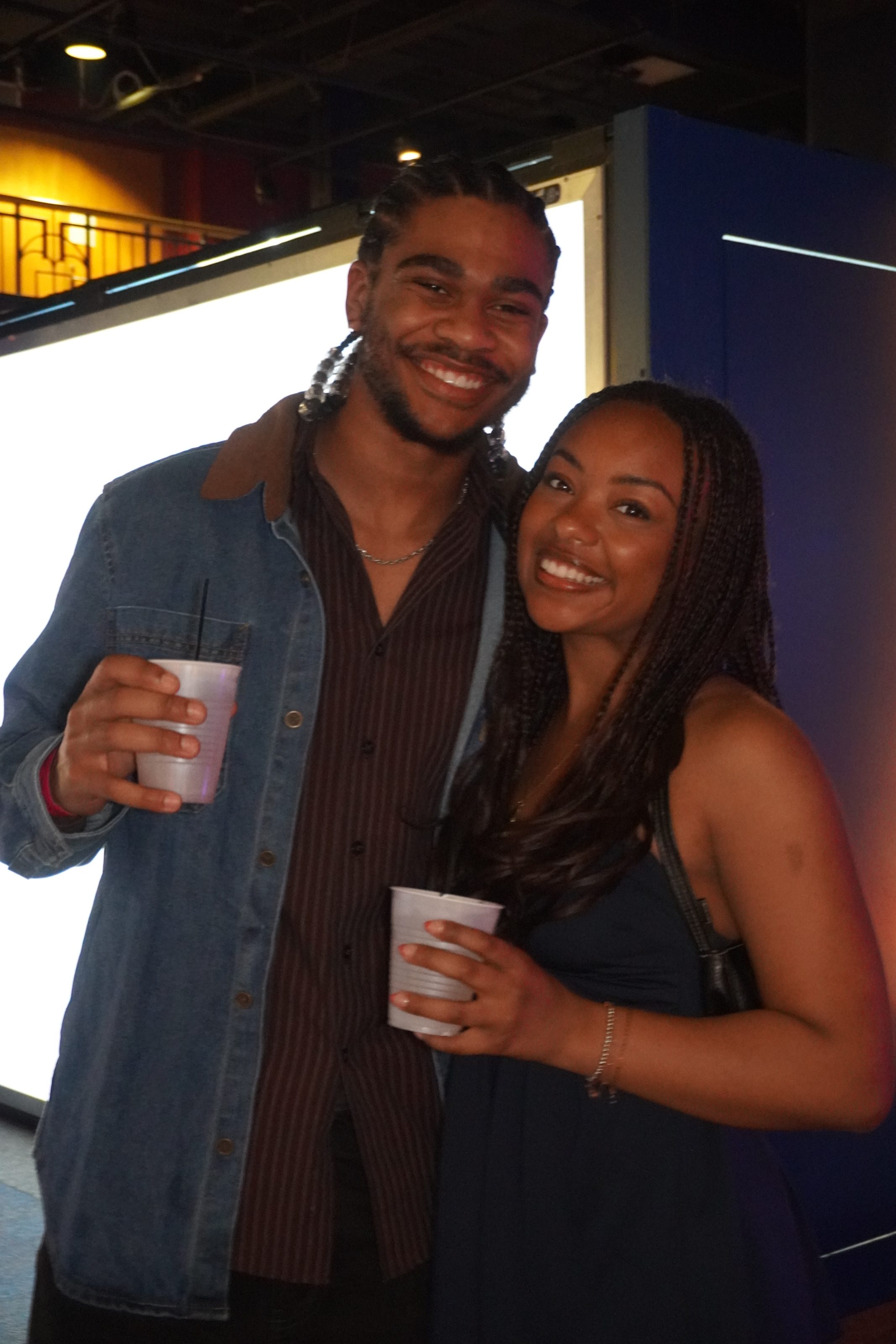 Two adults smiling with drinks at a children's science center exhibit during an evening event.