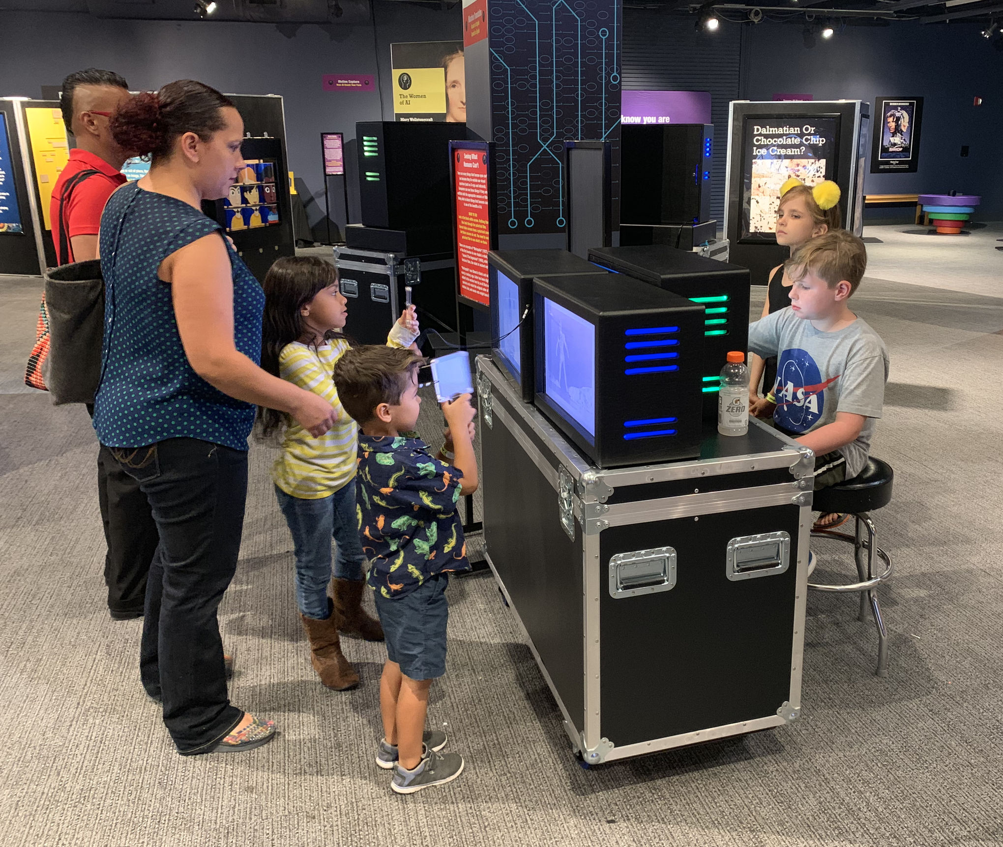 Kids and a parent explore hands-on STEM exhibit with interactive screens at a children's science center